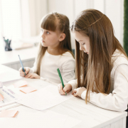 Dues nenes concentrades fent els deures juntes en una aula, simbolitzant l’aprenentatge compartit i l’acompanyament educatiu.