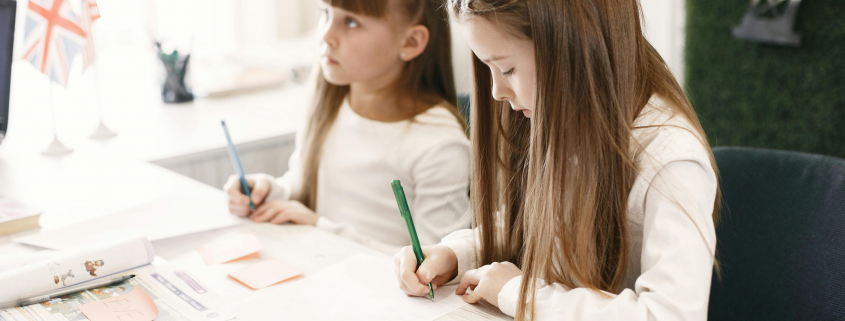 Dues nenes concentrades fent els deures juntes en una aula, simbolitzant l’aprenentatge compartit i l’acompanyament educatiu.